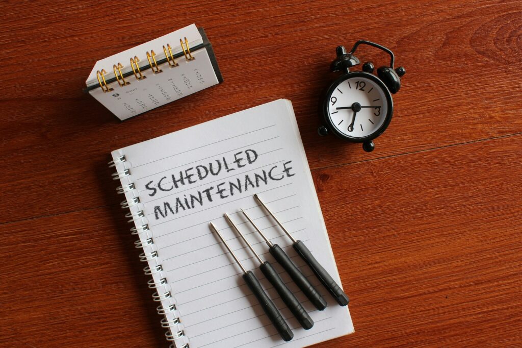 Calendar, alarm clock, screwdriver and book with text SCHEDULED MAINTENANCE.