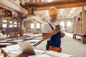 Cheerful builder using smartphone at construction site