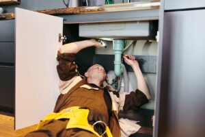 Young plumber fixing new pipe under sink with wrench