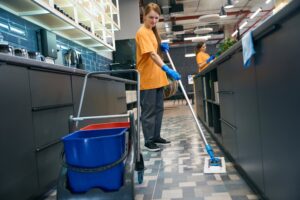 Young woman cleaning the floor with a mop, her colleague is in the background